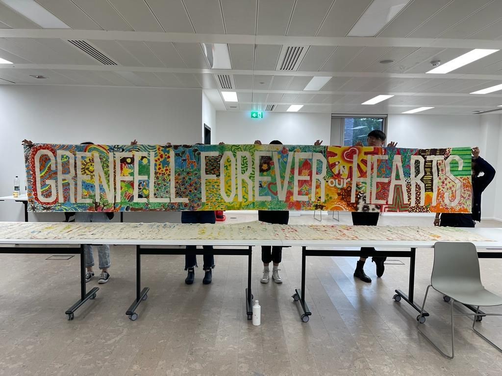 A group of people holding up a banner with the words Grenfell forever in our hearts